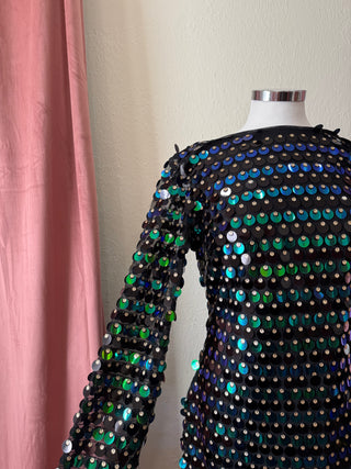 Mannequin wearing a black sequin dress with colorful beads against a pink curtain.