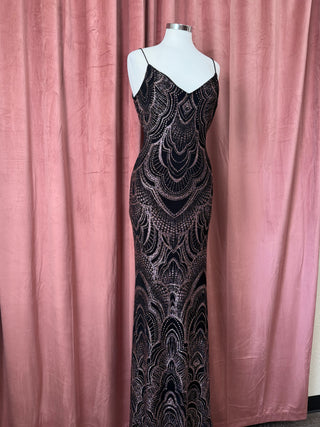 Black evening gown with intricate patterns on a mannequin against a pink curtain background