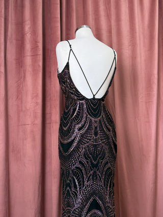 Mannequin wearing a black and gold patterned evening gown against a pink curtain.