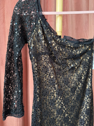 Black sequin dress on a wooden hanger against a pink background